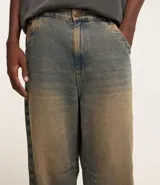 Pantalón super baggy de jeans con lavado dirty en tonos tierra, cintura con trabilla, cierre tradicional, bolsillos y bordado en el bolsillo trasero.