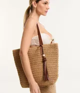 Bolso de playa tejido en paja de papel color marrón claro, con correa de hombro en material sintético color marrón. Incluye cierre a presión y detalle de borla colgante. Marca Bossa Nossa.