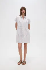 Vestido corto con cuello camisero, de corte holgado y mangas cortas. Presenta un diseño a rayas verticales en tonos beige y blanco, con volados en la falda y cierre frontal con botones.
