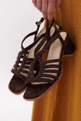 Sandalia de cuero color marrón oscuro con taco ancho y tiras trenzadas que cubren el empeine. Posee tira ajustable con hebilla en el tobillo.