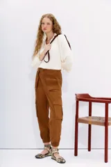 Pantalón cargo color marrón, de corte relajado con ajuste en los tobillos. Presenta bolsillos laterales con solapa, cintura con botón y cierre, y elástico en la espalda.