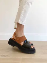 Sandalia de cuero en color camel y negro con diseño de tiras y suela gruesa.