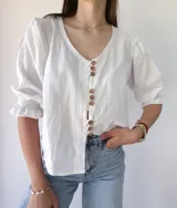 Camisa blanca de mangas 3/4 con detalle de volados en los puños y botones de madera.