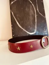 Cinturón de cuero color borgoña con apliques de estrellas doradas y hebilla metálica envejecida.