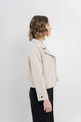 Chaqueta color beige de tela tipo gamuza con elastano, cuello solapa, manga larga con trabillas en hombro, bolsillos delanteros con cremallera metálica y cierre frontal con cremallera.