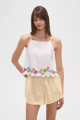 Top de algodón blanco con breteles finos regulables y escote cuadrado. Presenta un diseño holgado con bordado floral multicolor en el ruedo y terminación festoneada.