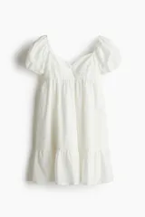 Vestido corto blanco de tejido liviano con escote corazón, mangas cortas abullonadas y elástico fino en hombros y puños. Espalda fruncida y corte ajustado en el busto con costura fruncida debajo. Pollera con leve vuelo y costura fruncida en el bajo.