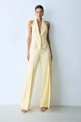 Pantalón de vestir color amarillo pastel, de corte recto y tiro alto. Presenta una capa superpuesta en la parte delantera, bolsillos laterales y traseros, y cierre con gancho.