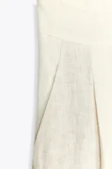 Pantalón culotte color crudo, de tiro medio, confeccionado en lino. Presenta bolsillos laterales, pinzas delanteras, pierna ancha y cierre frontal con cremallera, botón y ganchos metálicos.