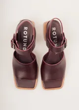Sandalias negras de cuero con diseño minimalista y taco ancho geométrico en tono madera. La capellada lisa aporta una estética depurada y moderna, mientras que la pulsera con hebilla metálica ajustable asegura un calce firme y confortable.
