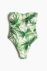 Traje de baño enterizo strapless con estampado de hojas de palmera en tonos de verde sobre fondo blanco. Tiene detalle metálico en el centro del busto, copas con relleno extraíble, reborde de silicona en la parte superior y corte alto en las piernas.