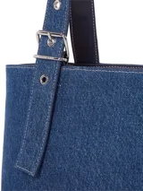 Cartera tipo tote confeccionada en tejido denim azul de Tommy Jeans. Presenta asas de hombro ajustables con hebillas metálicas y ojalillos, un compartimento principal y el logo de la bandera de Tommy Jeans en una placa metálica frontal.