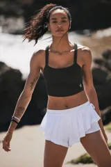 Top deportivo ajustado color negro, con escote redondo al frente y espalda cruzada. Presenta un dobladillo redondo que termina justo por encima de la cintura.