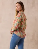 Blusa de gasa estampada a rayas verticales en tonos celeste, lila, naranja y marrón. Tiene cuello a la base con escote en V y botones. Delantera con bolsillo aplicado. Largo de manga regulable con presilla y botón. Terminación anudada opcional.