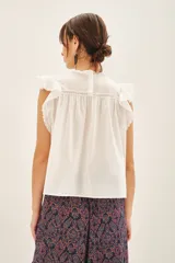 Camisa blanca de algodón con detalles de puntilla en el canesú, volados con terminación de puntilla en las mangas y cartera de botones en la parte superior de la espalda.