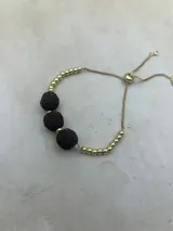 Pulsera dorada con tres piedras volcánicas negras y cierre corredizo.
