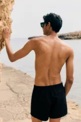 Short de baño negro de tela con tajos laterales cortos, elástico en la cintura con cordón ajustable, bolsillos laterales y bolsillo trasero con cierre autoadherente. Suspensor interior de malla.