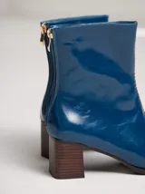 Botas de cuero charol negro con caña media y punta cuadrada. Cuentan con cierre trasero, tirador y bordado contrastante en el empeine. El taco es de madera y la suela de goma.