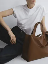 Bolso negro tipo tote bag con doble asa corta y correa larga extraíble.