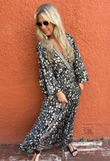 Vestido largo de manga larga, con escote en V y estampado floral en tonos negro, beige y gris. Presenta un detalle de borde estampado en la parte inferior de la falda.