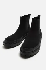 Bota Chelsea negra de cuero con acabado serraje, caña baja, puntera redondeada, tirador trasero y suela track con volumen.