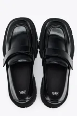 Zapato tipo mocasín negro con plataforma y suela track. Presenta tira ajustable adherente y tirador trasero.