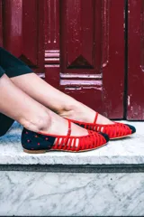 Bailarinas de piel bicolor, con pulsera y múltiples calados. La parte delantera lleva una rejilla transparente roja. La punta y el talón son de terciopelo de seda negro con lunares rojos.