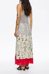 Falda midi de corte línea A, con estampado moteado en tonos beige y marrón oscuro. Presenta un forro rojo que asoma en el bajo y una capa superior de tejido ligero con un patrón similar al moteado.