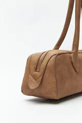 Cartera baguette color marrón claro, confeccionada en símil cuero con formato cilíndrico y doble asa corta.
