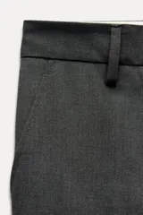 Pantalón de vestir gris oscuro de tiro bajo, con trabillas en la cintura, bolsillos delanteros y traseros, raya planchada y pierna recta.