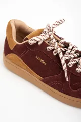 Zapatilla de cuero con capellada de gamuza en tonos borgoña y camel, con suela de goma color caramelo. Cordones trenzados en blanco y marrón.