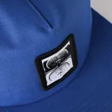 Gorra de visera plana color azul con parche frontal negro que contiene dos imágenes en blanco y negro, posiblemente resonancias magnéticas o escaneos cerebrales.