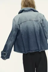 Chaqueta de denim celeste con cuello alto, manga larga con trabilla y bolsillos laterales. Presenta detalle de pliegues en la espalda y cierre frontal con botones ocultos.