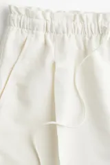 Short blanco de lino con cintura elastizada y cordón ajustable. Presenta pliegues frontales, bolsillos al bies y corte holgado.