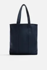 Bolso tipo shopper color azul marino, fabricado en tejido de algodón. Tiene doble asa de mano y un bolsillo plano en el interior.