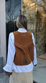 Chaleco marrón de cuero descarne con terminación en picos, tachas metálicas y flecos en la espalda.