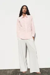 Camisa manga larga color rosa pálido con cuello solapa y cierre frontal con botones. Detalle de bordados perforados engomados con motivos florales. Corte recto.
