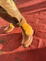 Botas de cuero marrón con paneles de corderito en color beige en la caña. Cuentan con una suela de goma tipo track en tono tostado y cierre de cremallera lateral.