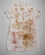 Vestido línea A de algodón cambray, teñido a mano con técnica botánica, resultando en un estampado único con manchas y salpicaduras en tonos rosados, amarillos suaves y terrosos. Presenta manga corta, bolsillos laterales, cuello limpio y una tabla frontal que añade estructura.