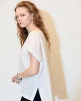 Top blanco de lino melange, de silueta relajada, con cuello bote, espalda con costura en el centro y tajos en los laterales del ruedo.