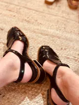 Sandalias de cuero charol negro con tiras anchas y hebilla al tobillo.