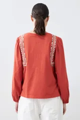 Remera blanca de estilo boho con bordados en el escote y mangas largas. Presenta escote en V con lazos y borlas. Corte recto y holgado.