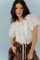Blusa blanca con bordado calado, mangas cortas abullonadas y lazos frontales.