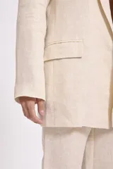 Blazer color crema con textura de lurex, solapas clásicas, corte recto y bolsillos delanteros.