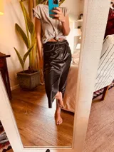 Pollera midi de cuero negro con abertura frontal y costuras blancas a contraste.