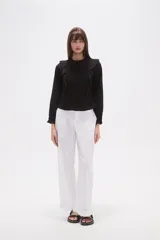 Blusa de algodón color negro con cuello a la base y detalle de volados en el frente. Posee mangas largas con puños elásticos y un panel frontal con textura fruncida.