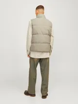 Chaleco acolchado sin mangas color gris topo, con cuello alto y cierre de cremallera. Tiene bolsillos frontales y relleno de fibra sintética.