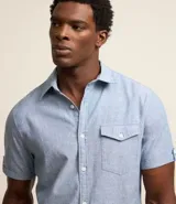 Camisa de hombre de manga corta en lino color blanco, con cuello clásico, botonadura frontal y bolsillo de parche en el pecho. Corte recto.