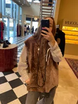 Chaleco de cuero genuino con textura de pelo en color marrón, diseño cruzado con cierre de botón lateral y cuello solapa.