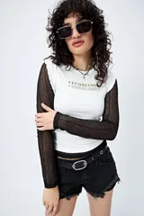 Remera blanca de algodón, poliéster y elastano con mangas largas de tul negro. Estampa frontal con la palabra 'Fearless' en verde. Corte entallado y terminaciones con volados sutiles.